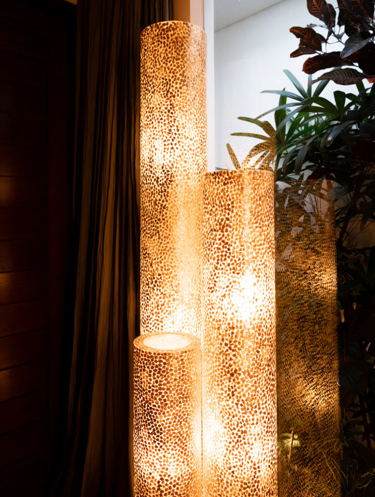 A set of illuminated Wangi Gold floor lamps from Light House Design in a tropical environment