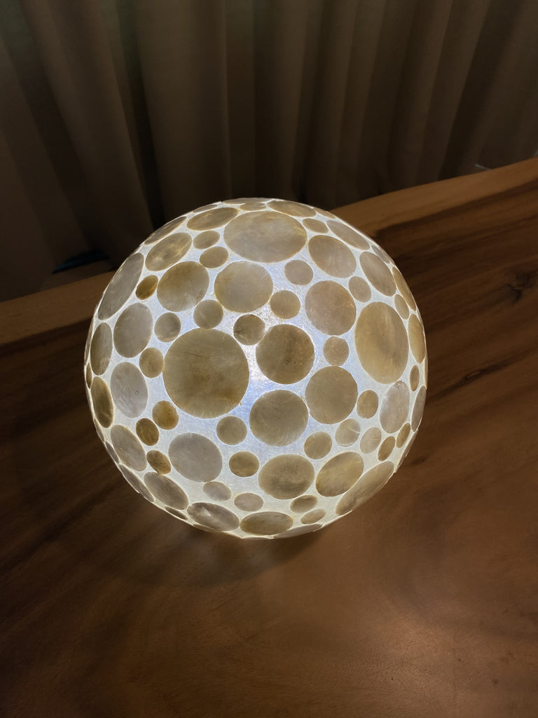 White Coin sphere table lamp glowing on a wooden table