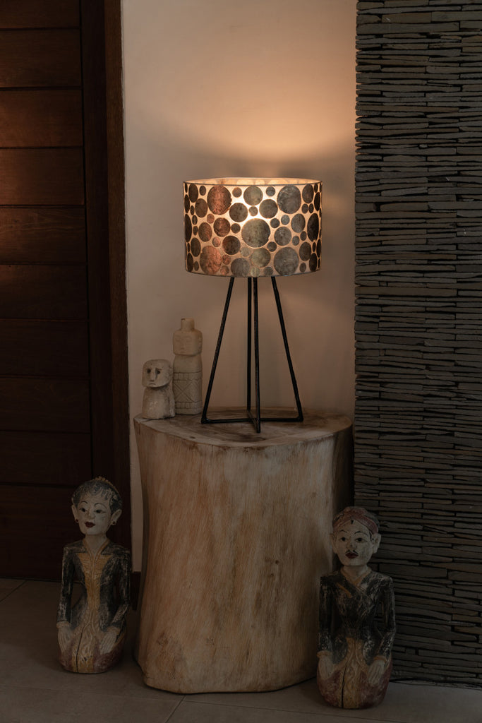 Very decorative table lamp in Gold Coin design standing on a table. Next to it are old statues made from wood