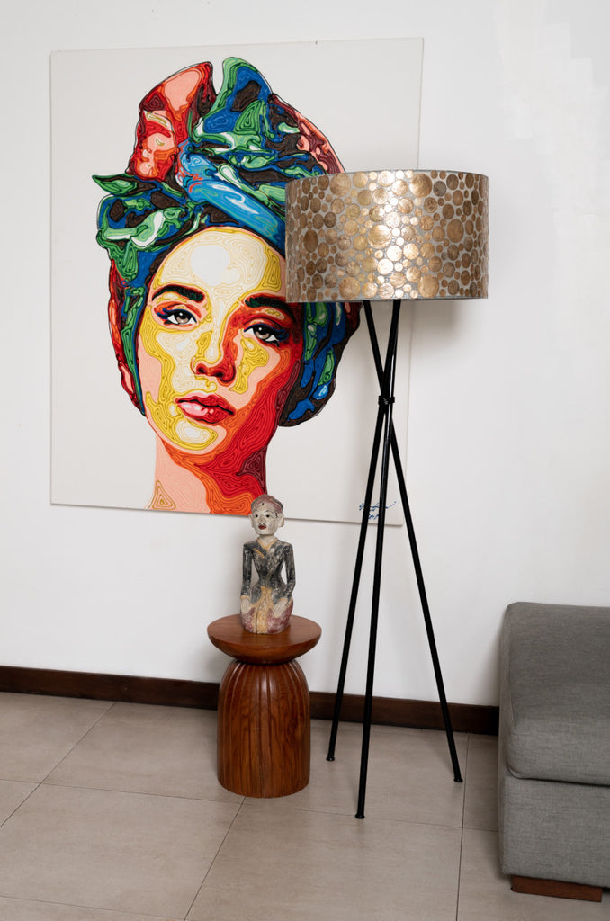 Gold Coin floor lamp with Shade standing Infront a picture. The floor lamp has a black body and a shade in Gold Coin Design