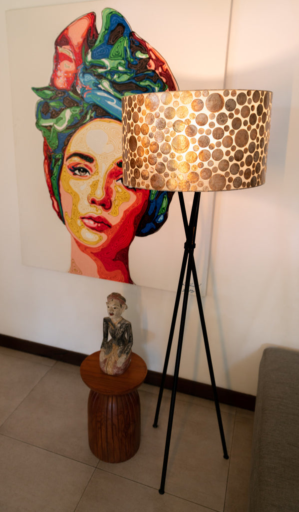 Gold Coin floor lamp with Shade standing Infront a picture. The floor lamp has a black body and a shade in Gold Coin Design