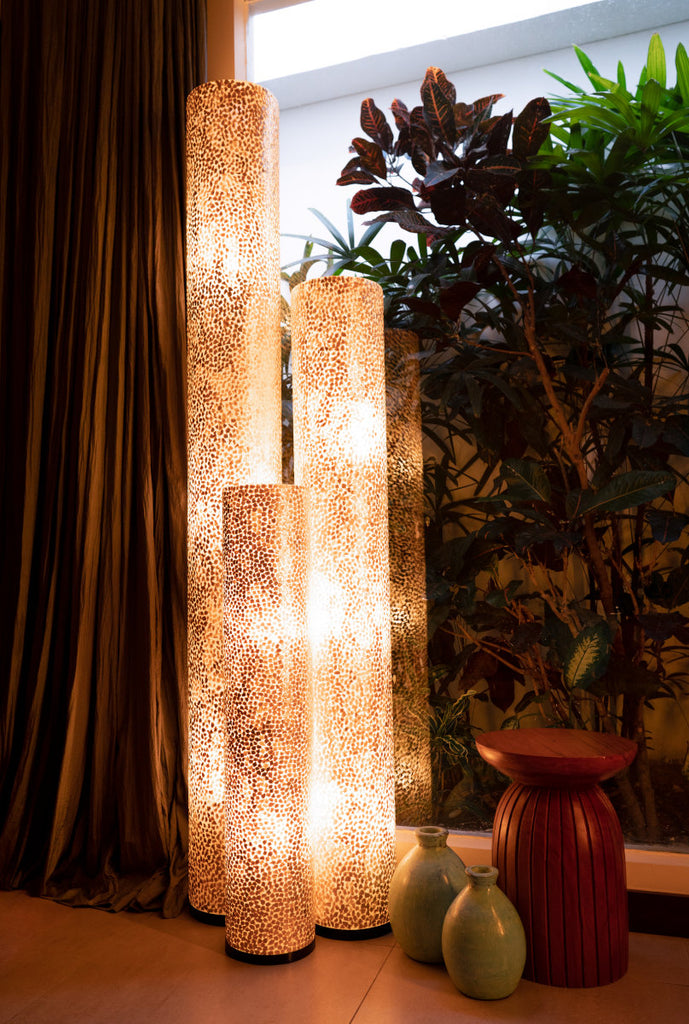 A set of illuminated Wangi Gold floor lamps from Light House Design in a tropical environment